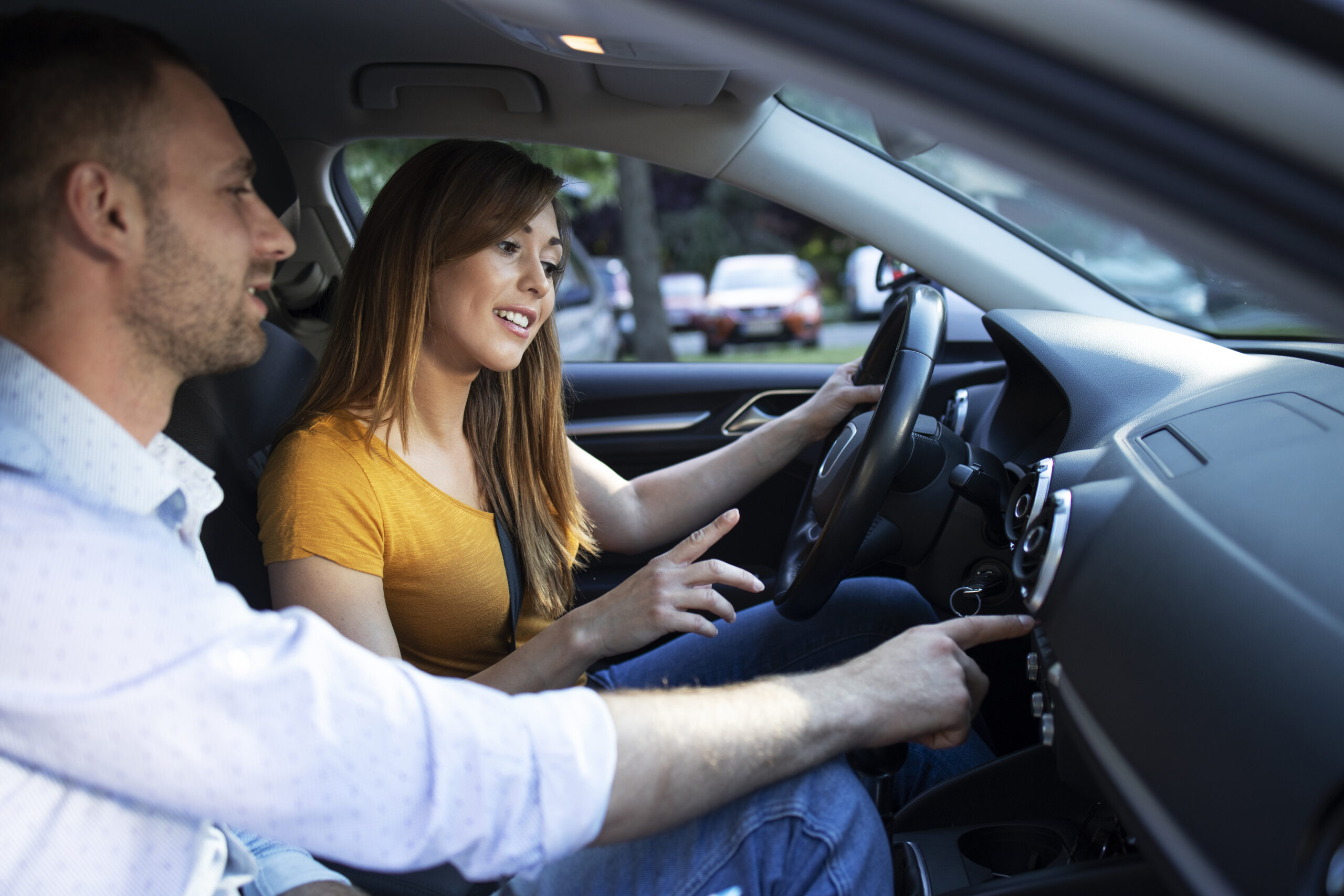 driving instructor showing vehicle dashboard and buttons to the student taking driving lessons.